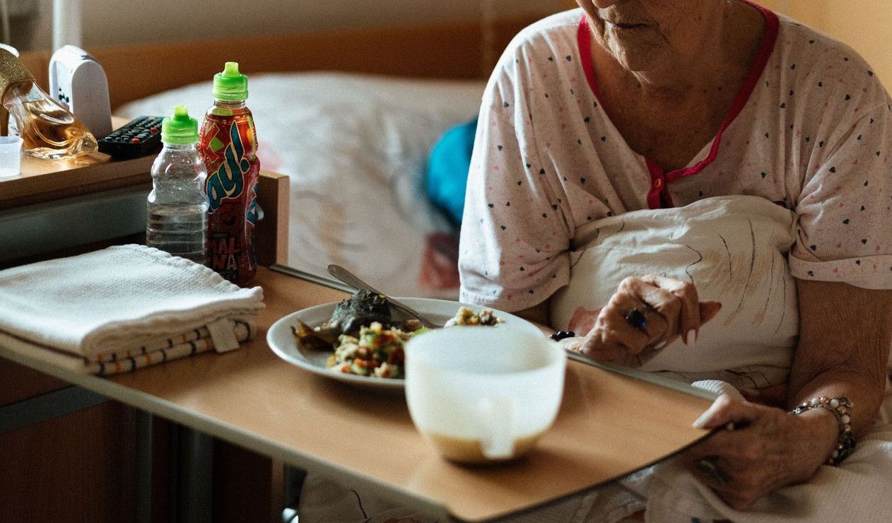 Elderly woman enjoying a meal in a cozy retirement home setting.
