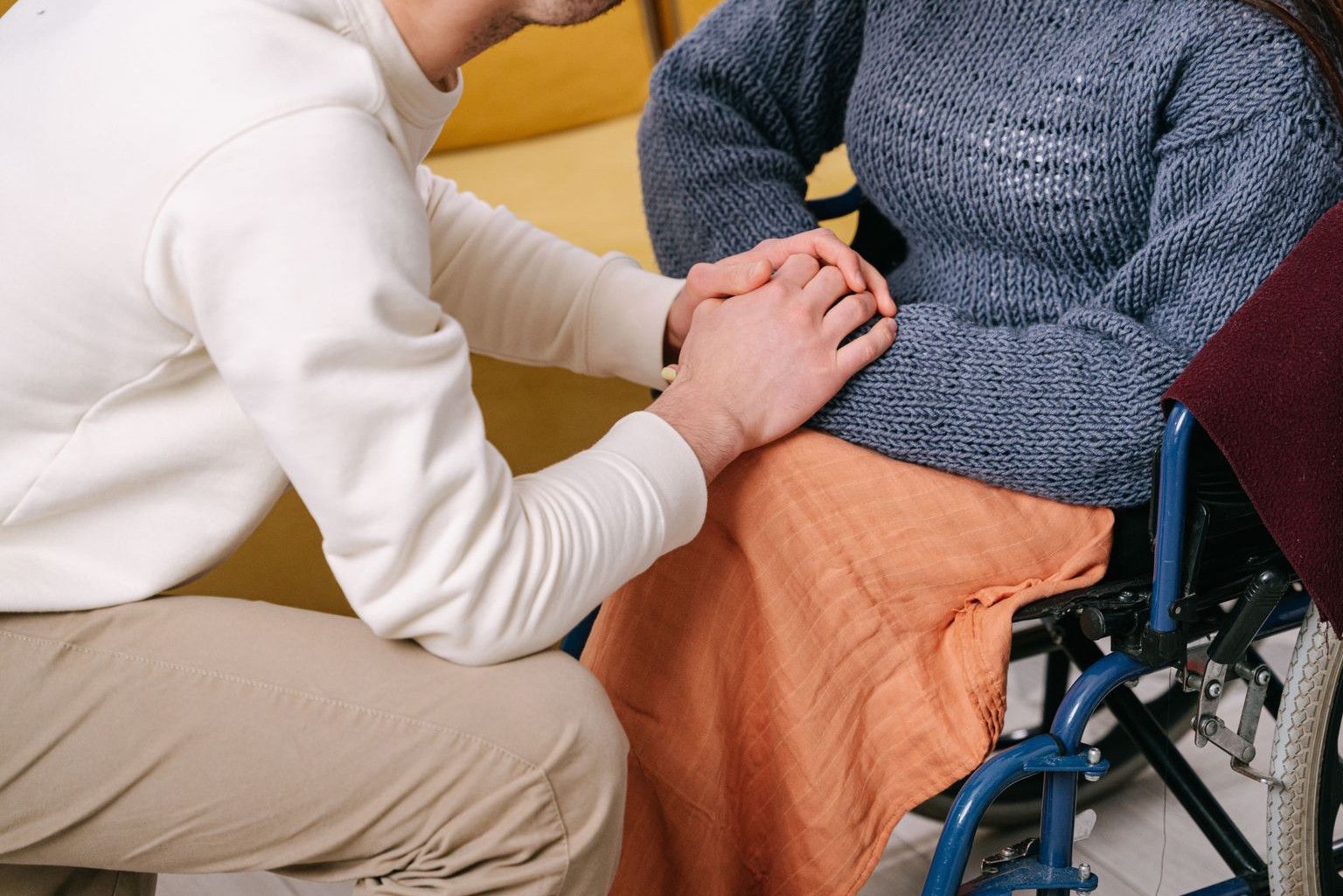Man providing care and support to woman in a wheelchair indoors.